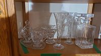 Full set of crystal and glass items arranged on a wooden shelf including decanter, vases, cream and sugar set with platter, and additional serving dish.