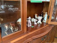 Front angled view inside wooden cabinet showing various ceramic dog figurines including poodles and beagles displayed on shelves.
