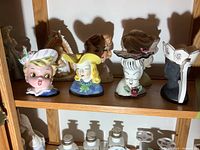 Six head vases on wooden shelf, various colors and hat styles
