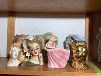 Six ceramic lady head vases and figurines displayed on wooden shelf