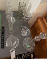 Eight pieces of clear patterned glass: four vases, two decanters, and two candy dishes on a table surface.