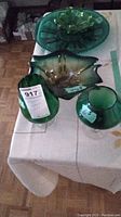 Photo of all five green glass items arranged on a table including two stemware glasses, one art glass dish, one ashtray, and one round serving tray.