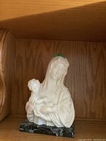 White mother and child figure on black marble base on wooden shelf