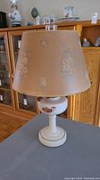 Full view of the vintage kerosene lamp with beige floral lampshade on, showing ceramic base and overall height.