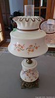 Front view of vintage glass hurricane lamp with orange floral design, wavy top rim, and clear glass chimney.
