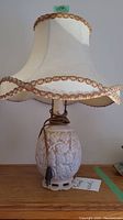 Full view of vintage ceramic lamp with removable cream-colored, fabric lamp shade featuring decorative braid trim on scalloped edges.