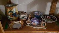 Overview of assortment of lusterware items on shelf including painted vase, teapot set, bowls, spoons.