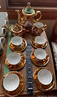 Overview of entire set showing six cups with saucers, coffee pot, creamer, and sugar bowl on wooden surface with measuring tape for scale.