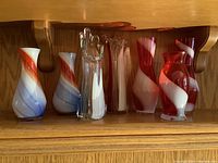 Full set of seven glass vases with swirl patterns in red, white, and blue, displayed on a wooden shelf.