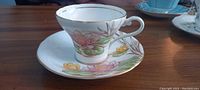Side view of Aynsley vintage bone china tea cup and saucer with hand painted Water Lily floral pattern in pink, yellow, green and brown.