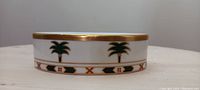 Side view of oval soap dish showing gold trim and palm tree pattern on white porcelain.