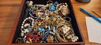 Top view of a collection of mixed costume jewellery including chains, beads, and brooches piled in a black velvet tray.