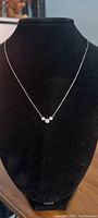 Front view of necklace displayed on a black bust, showing three bezel-set round diamonds on a fine platinum chain.