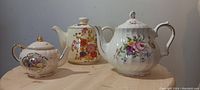 Three Sadler teapots with floral designs photographed on a wooden surface.