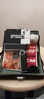Side view of black and white Sankyo 35mm movie camera placed inside its open carrying case, with instruction booklets partially visible underneath.