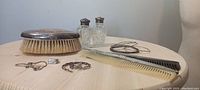 Objects on wood table showing multiple silver and crystal/salt and pepper items, comb, rings, bracelets, and brush.