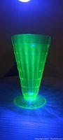 Photo of a uranium glass sundae cup glowing bright green under 395nm ultraviolet light, highlighting its fluorescent properties and overall shape.