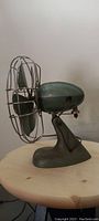 Side view of vintage Seabreeze table fan showing metal blades, wire cage, green housing, and base.