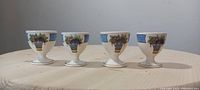 Four Wedgwood Etruria soft boiled egg cradles arranged in a row on a light wood table, showing the outward design with blue basket of fruits and vegetables decoration.