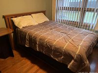 Wooden bed frame with mattress bedding and pillows placed, positioned near a window with vertical blinds.
