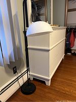 Full view of the black metal arc floor lamp with white dome-shaped shade positioned beside a white dresser and near a window with blinds.