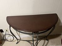 Photo of half circle table from an angle showing brown wooden top and metal base with decorative element.