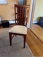 Close-up view of a wooden dining chair with slatted backrest and cream upholstered seat.