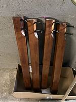 Disassembled wooden table legs stored upright in a box, medium brown finish with black metal hardware attached for assembly.