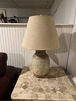 Photo of vintage ceramic table lamp with beige crackle glaze base and cream fabric lampshade on side table, showing overall condition and size in room context.