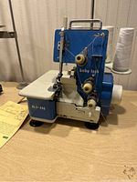 Front and side view of Baby Lock BL3-406 sewing machine with thread spools attached, placed on a table with an instruction sheet visible.