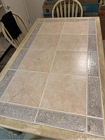 Top view of the rectangular tile top dining table showing beige and brown decorative tiles with some cracks visible.