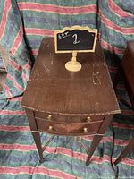 Left side wooden side table with visible scratches and minor wear on the tabletop, two drawers with brass knob handles, tapered legs.
