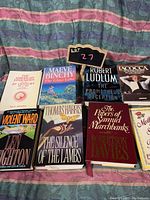 Photo showing 10 assorted adult hardcover books, titles visible, arranged on fabric background.