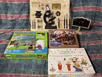 Lot overview showing vintage microscope set, dinosaur puzzle tin, floor puzzle box, and Caillou logic game box.