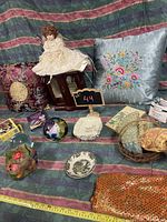 Wide shot of lot showing pillows, doll, decorative glass orbs, basket with scarves, books, jewelry box, angel figurine, decorative plates, and decorative fabric pouch.