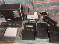 Photo showing front view of most items in the lot including two PS2 consoles, desktop CPU, keyboard, music player, Coors Light device, DVD player and remotes.