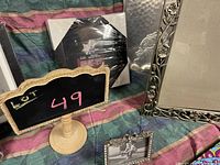 Photo showing a silver ornate photo frame, a small silver frame with grayscale horse photo, and a black octagonal photo frame wrapped in plastic with a small wooden stand sign showing number 49
