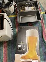 Overview of the mini crockpot, white toaster, metal bread pans, and boxed beer boot glass on a striped cloth