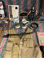 Photo showing tan tactical survival vest with ammunition belt, two Pilsner collectible mugs, Stone Cold Steve Austin action figure, survival book, and a small chalkboard with number 72.