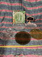 Full view of six platters including clear, gold-toned, and dark glass, arranged on fabric.