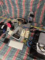 Photo showing Canon printer, white Mac keyboard, digital remote, various networking cables, phone cases, and small electronic items displayed on striped fabric background.