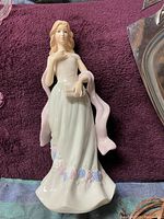 Porcelain figurine of woman in long white dress with pastel flowers, standing on purple towel background.