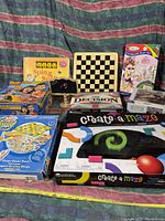 Photo showing an assortment of board games and puzzle boxes stacked on a fabric surface, various themes and sizes visible.
