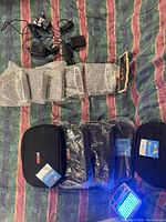 View of several GoLite light therapy units in bubble wrap alongside chargers and protective cases on a striped surface.