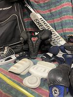 Photo showing lot with skates, sticks, shoulder pads, gloves, protective pads, and large black Sher-Wood bag