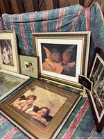 Five framed art prints arranged against fabric background, showing cherubic angels and landscape scenes.