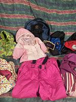 Photo showing multiple pieces of kids outerwear and a blue and black backpack laid out on a patterned fabric background.