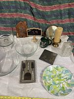View of various kitchen and dining items including glass bowls, cheese serving set, decorative plate, teapot, candlesticks, glass bottle, and metal tin