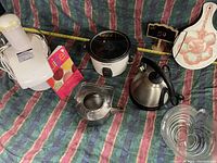 Photo showing electric juicer, recipe book, kettle, apple bowl, paper towel holder, and cutting board