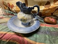 Pottery pitcher and bowl set in blue and cream with floral decoration on a fabric surface